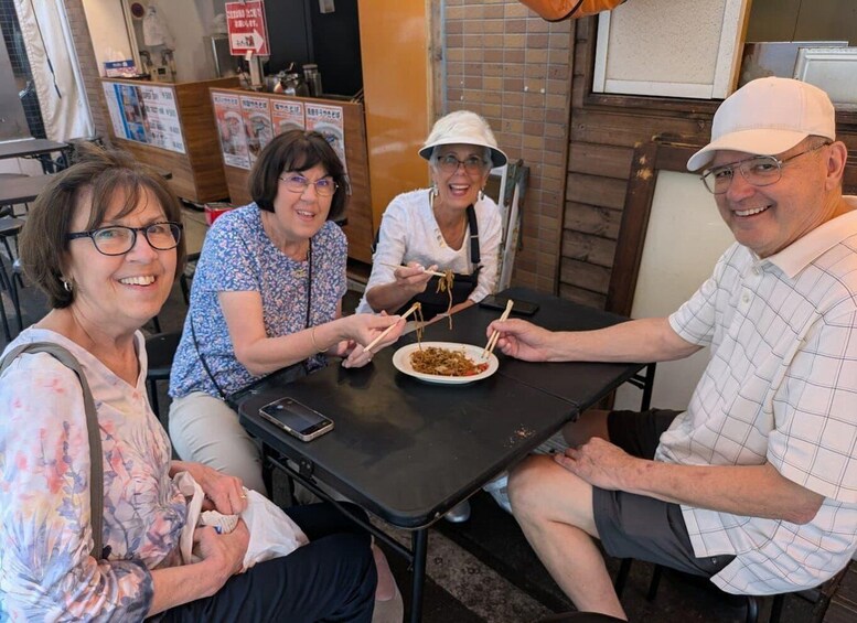 Three people seated at a table with a plate of food, a mobile phone, and a menu board in a restaurant. 3