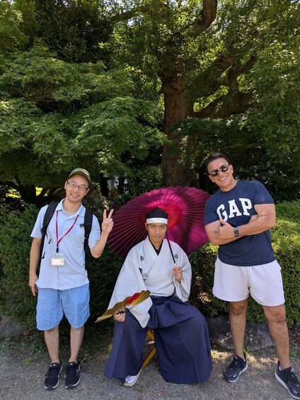 Three people in a park with trees and a bench. One person is holding an umbrella. 5