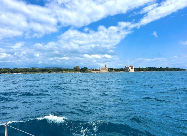 A coastal landscape with a clear sky, a body of water, and two prominent buildings on a small island. 3