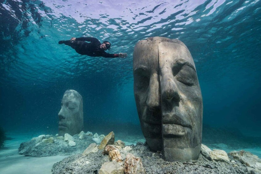 A diver swimming near large stone head sculptures underwater. 4