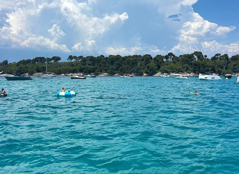A turquoise sea with boats, a person on a blue inflatable, and a tree-lined shore. 2