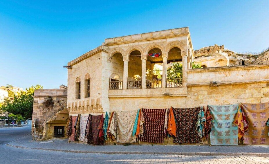 A historic building with arches and a balcony, with colorful textiles hanging outside. 1