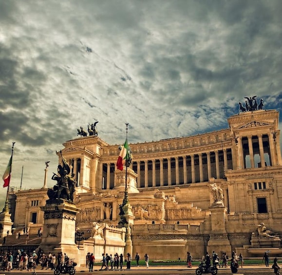 A grand neoclassical building with statues and columns, surrounded by people and flags. 1