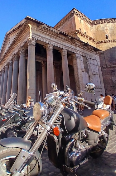 A classical building with columns and a paved area with parked motorcycles. 3