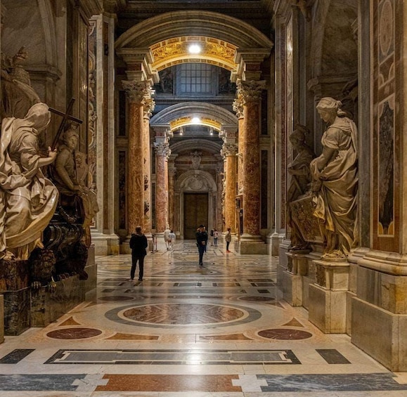 A grand hall with marble columns, statues, and a patterned floor. 2