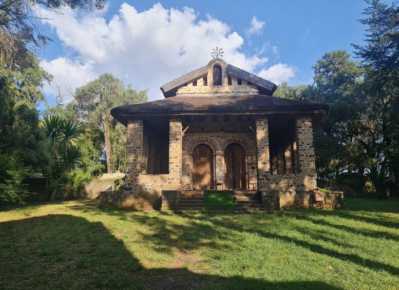 A stone structure with a central dome and arched doorways, surrounded by grass and trees. 3