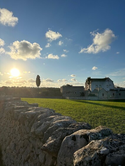 A stone wall, a grassy field, and a building with a tower under a clear sky. 2