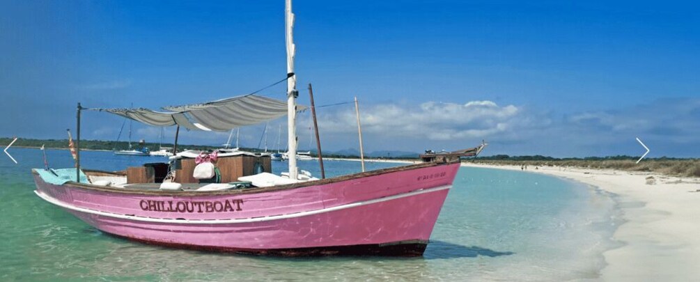 A pink boat named 'CHILLOUTBOAT' anchored near a sandy beach with clear turquoise water. 1