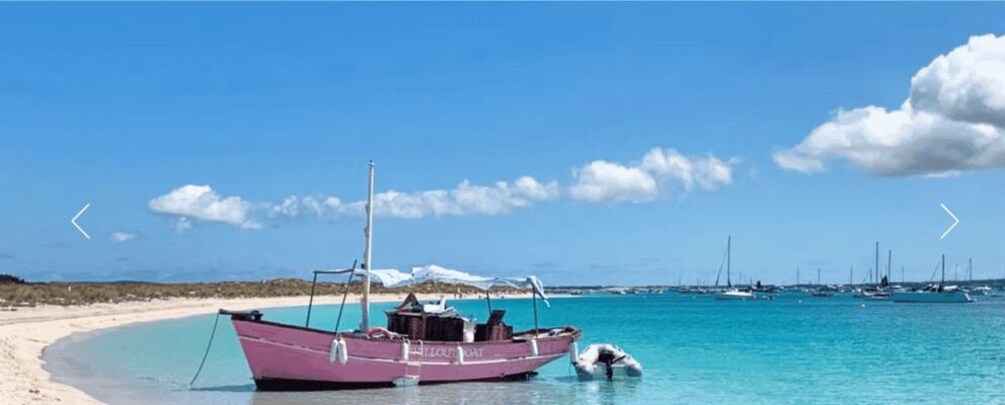 A pink boat on a sandy beach with clear turquoise water and a few sailboats in the distance. 3