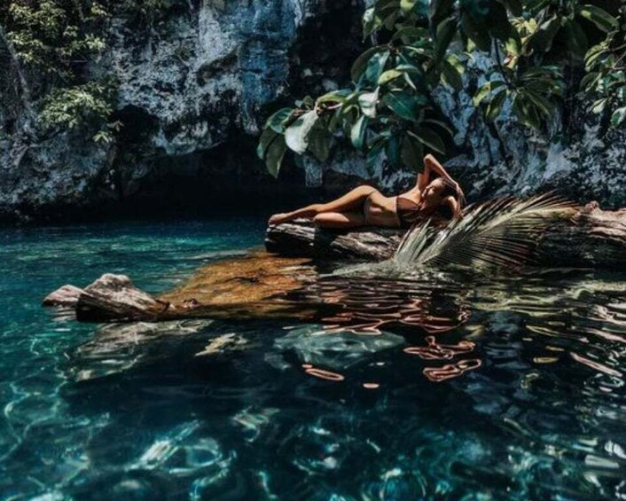 A person relaxing on a rock in clear water with a tropical backdrop. 1