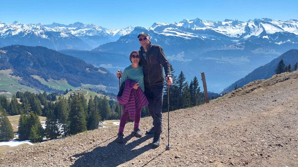 A person hiking with a child on a mountain trail, surrounded by snow-capped peaks and forested valleys. 1