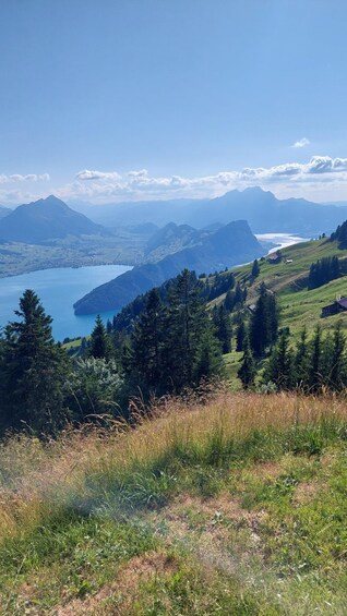 A mountainous landscape with a lake, dense forests, and distant peaks under a clear sky. 5