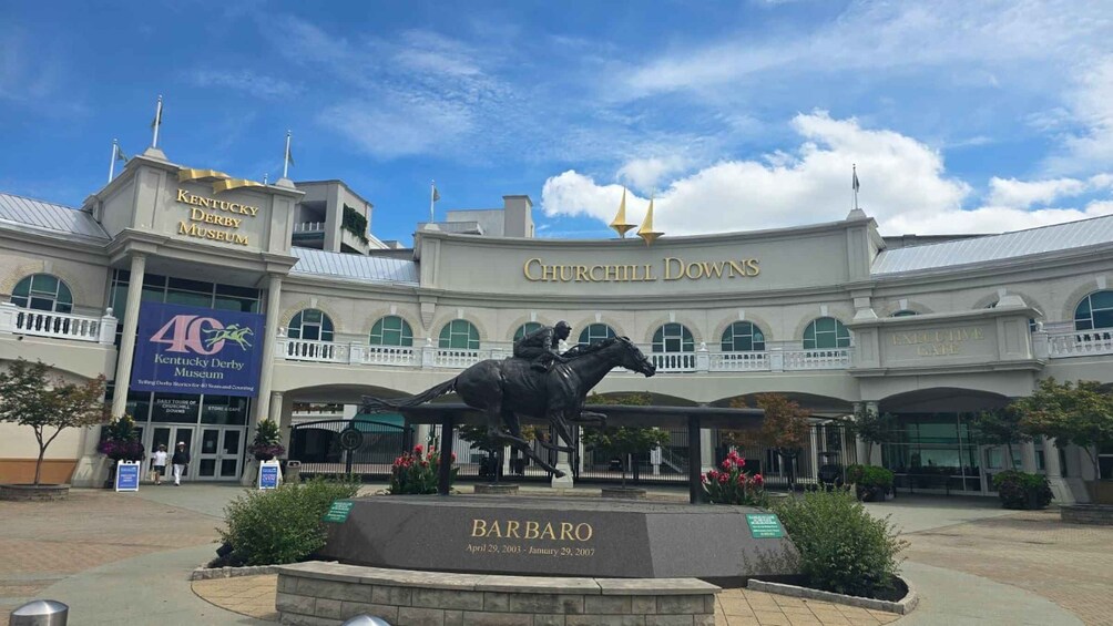 A statue of a horse rider in front of Churchill Downs, with Kentucky Derby Museum signage and a plaque for 'BARBARA' visible. 3