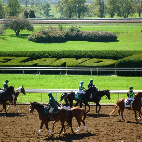 A horse race with jockeys on horses, a well-manicured track, and a green field in the background. 1