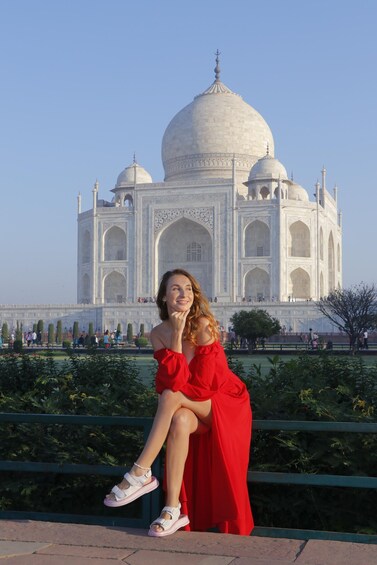 A person in a red dress sitting on a bench with the Taj Mahal in the background. 3