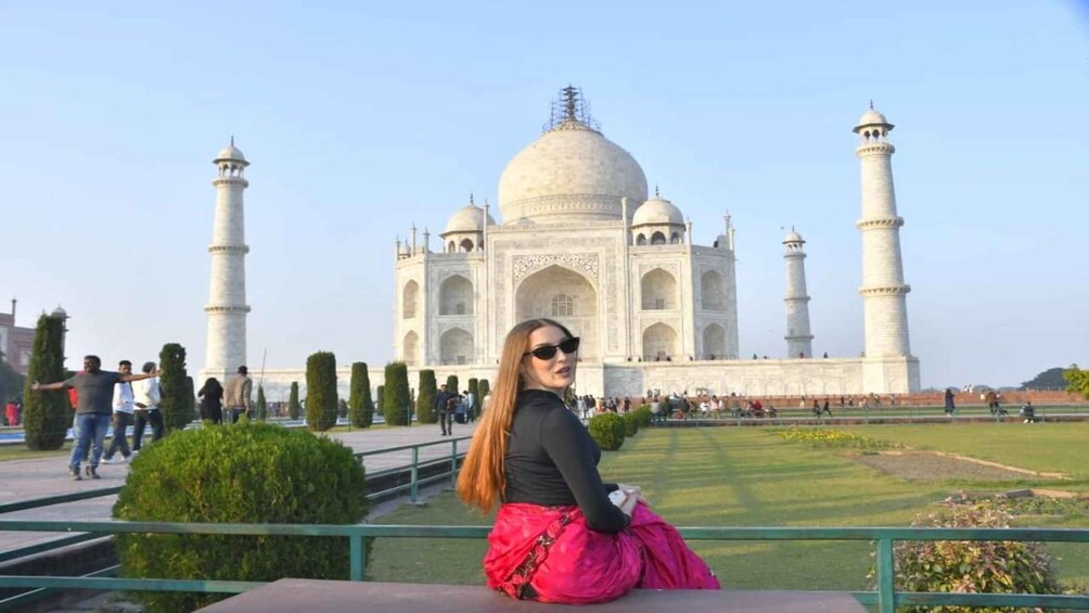 A person sitting in front of the Taj Mahal with its four minarets and central dome visible. 1