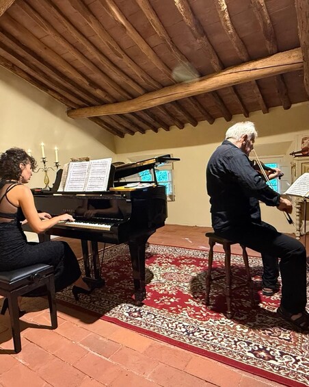 A woman playing a piano and a man playing a violin in a room with a wooden ceiling and patterned carpet. 1