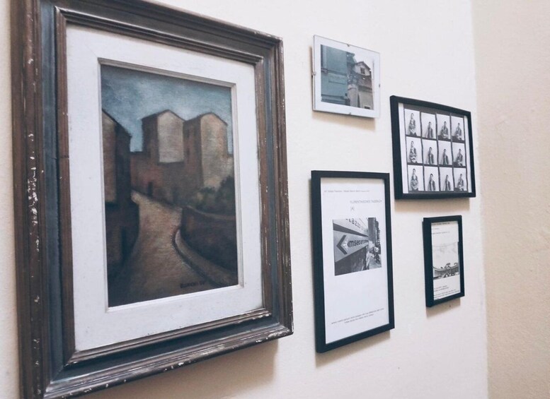 A wall with various framed artworks, including a landscape painting and several black-and-white photographs. 2