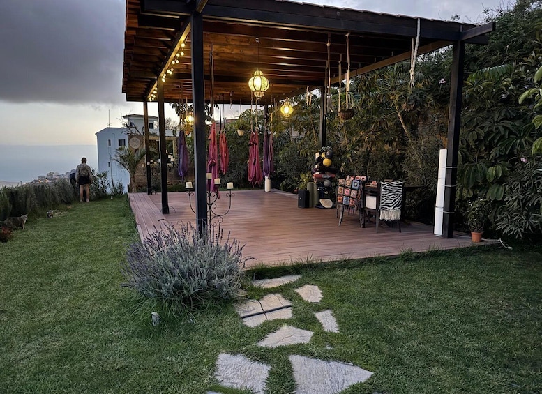 A covered outdoor patio with a wooden deck, hanging lights, and potted plants. 5