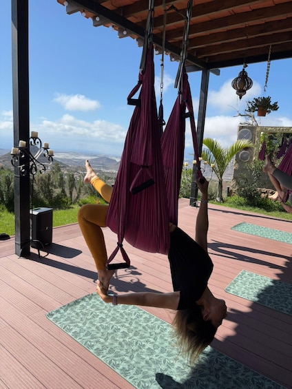 A person performing aerial yoga on a hammock in a scenic outdoor setting with a view of the landscape. 1