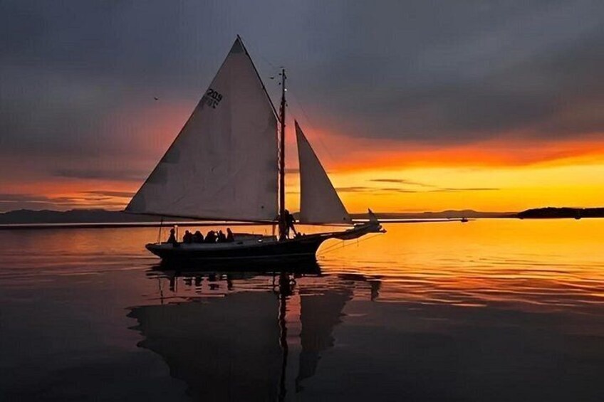 A sailboat with a triangular sail on calm water during sunset. 2