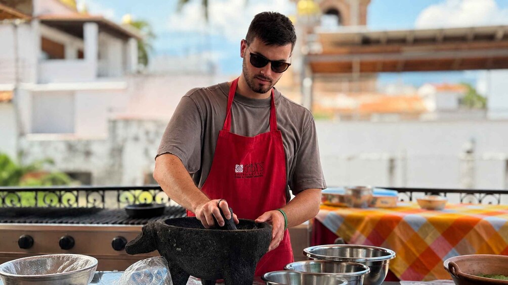 A person cooking outdoors, wearing a red apron, with cooking utensils and pots on a table. 2