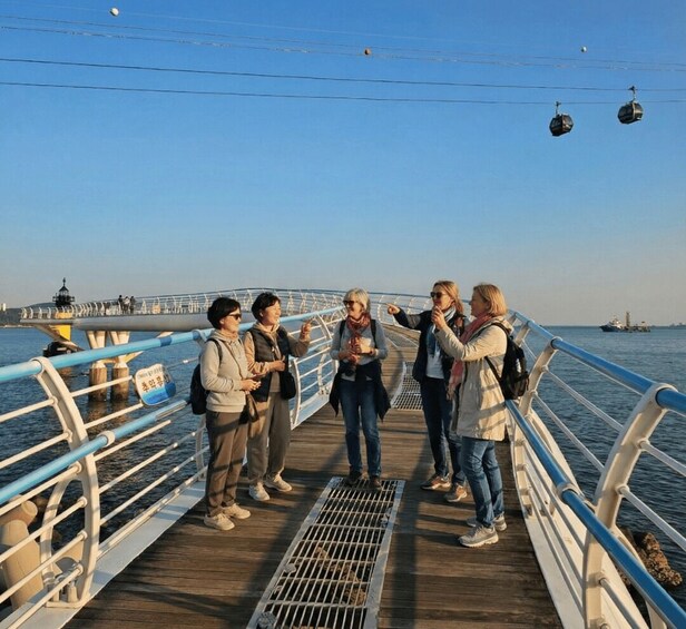 A group of people on a wooden boardwalk by the water, with a pier and a boat in the background. 4