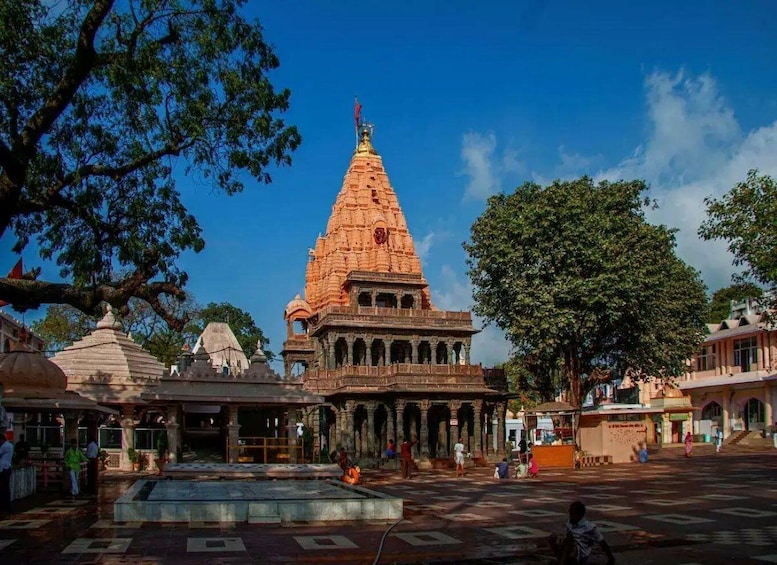 A temple with a large spire, surrounded by trees and a courtyard with people. 1