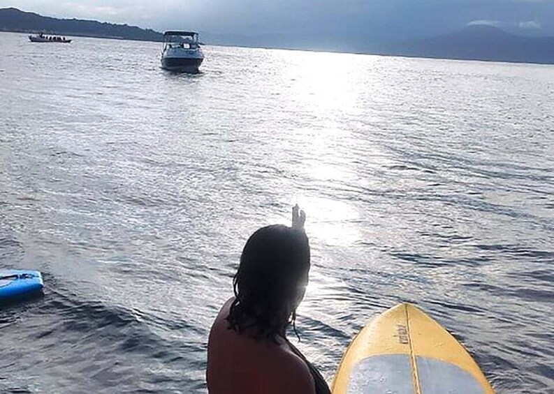 A person with a surfboard in the water, a boat in the distance, and a clear sky. 2