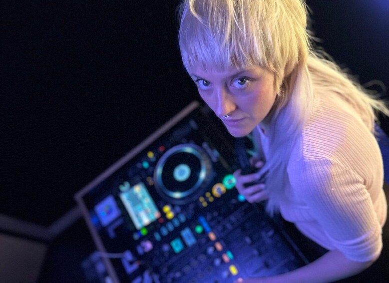 A person operating a DJ console with illuminated buttons and sliders. 5