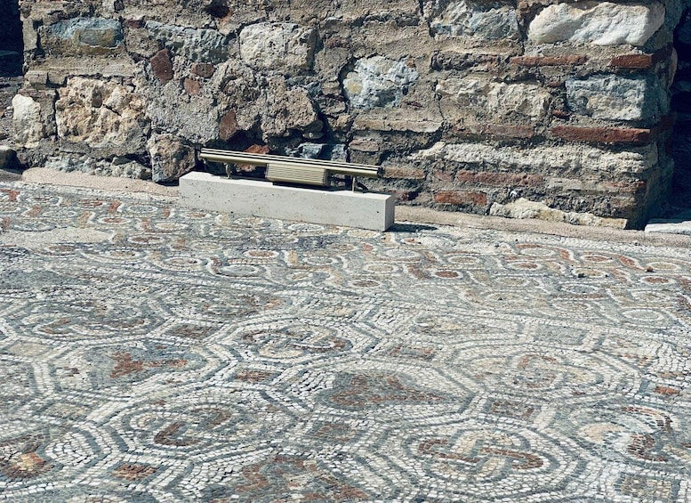 A mosaic floor with a stone wall in the background. 5