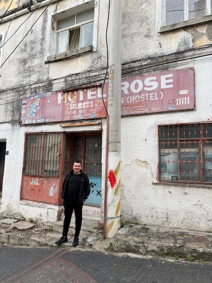 A man standing in front of a building with a sign that reads 'HOTEL ROSE (ROSTEL)'. 2
