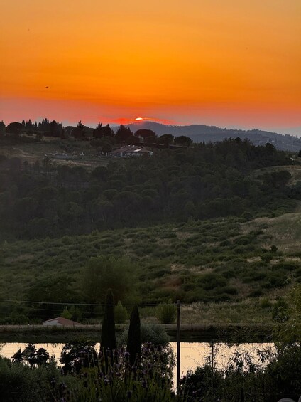 A sunset over a hilly landscape with a body of water in the foreground and a village in the distance. 2