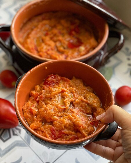 Two ceramic bowls filled with a chunky tomato-based dish, held by a hand. 3