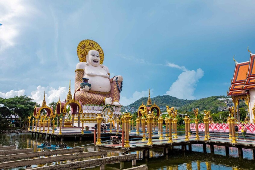 A large white Buddha statue with a golden halo, surrounded by ornate golden structures and a bridge over water. 2