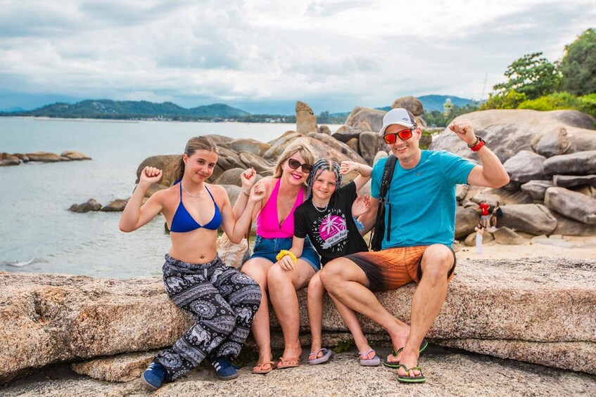 A group of people sitting on rocks by a body of water with mountains in the background. 1