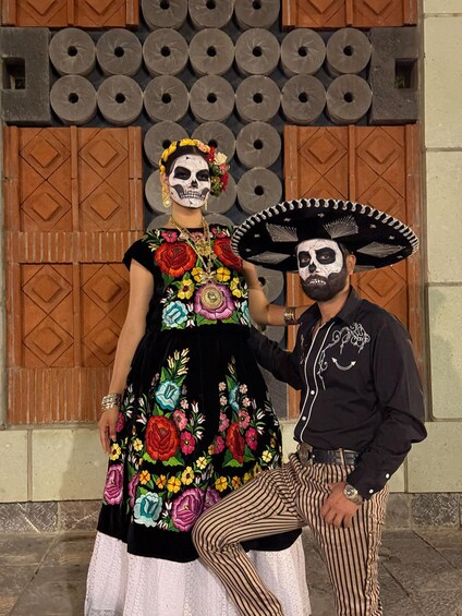 A person in a black and white face paint with a sombrero, and another in a colorful embroidered dress. 4
