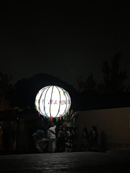 A brightly lit spherical structure with 'VIDA ENLA' written on it, surrounded by people. 2
