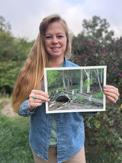 A person holding a painting of a forest scene with a bridge. 4