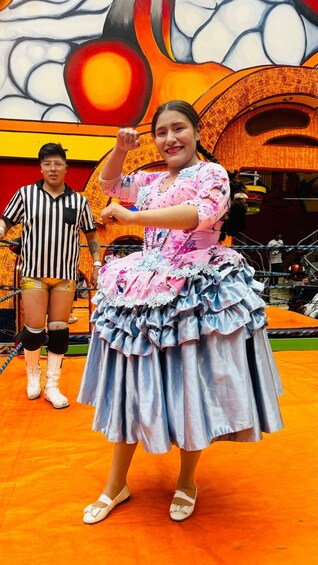 A person in a colorful dress standing on a stage with a referee in striped attire. 3