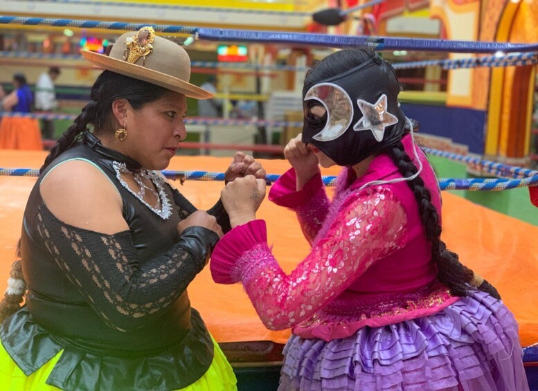 Two individuals in traditional attire, one wearing a hat and the other a mask, engaged in a wrestling match. 1