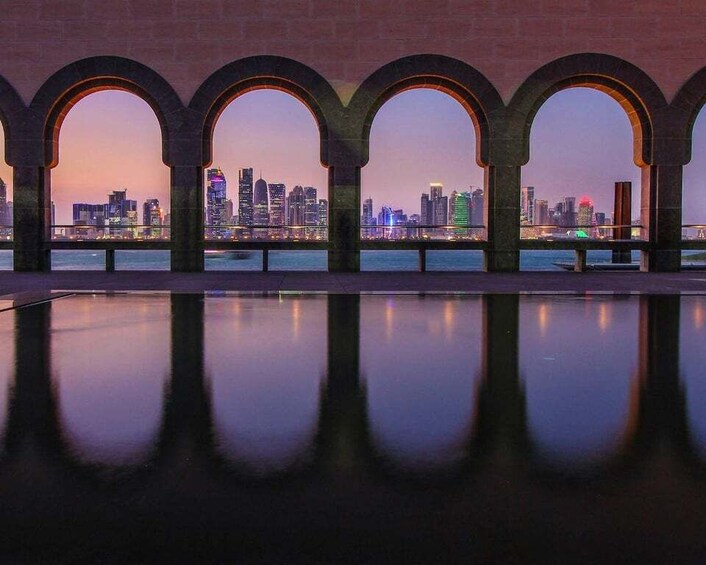 A city skyline at dusk reflected in a calm body of water, framed by arched structures. 4