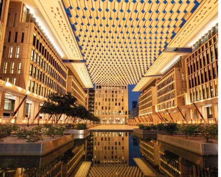 A modern building with a unique geometric ceiling design, a central reflective water feature, and surrounding greenery. 3