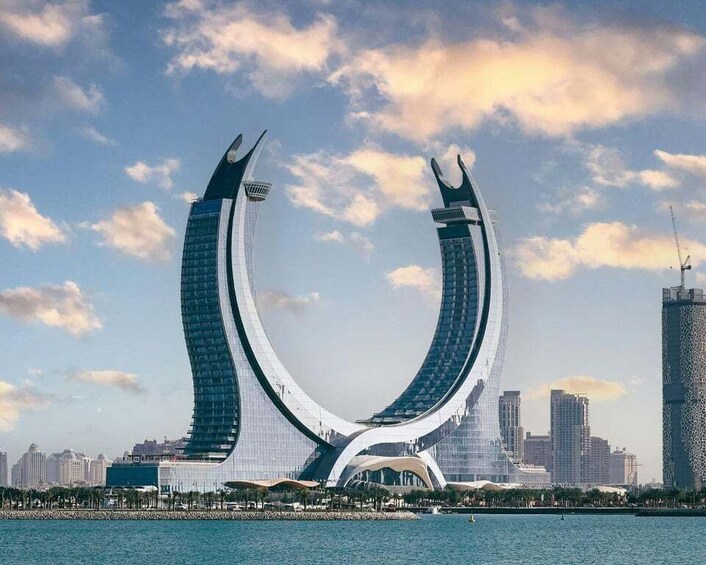 A distinctive curved building with a central archway, surrounded by a city skyline and a body of water. 2