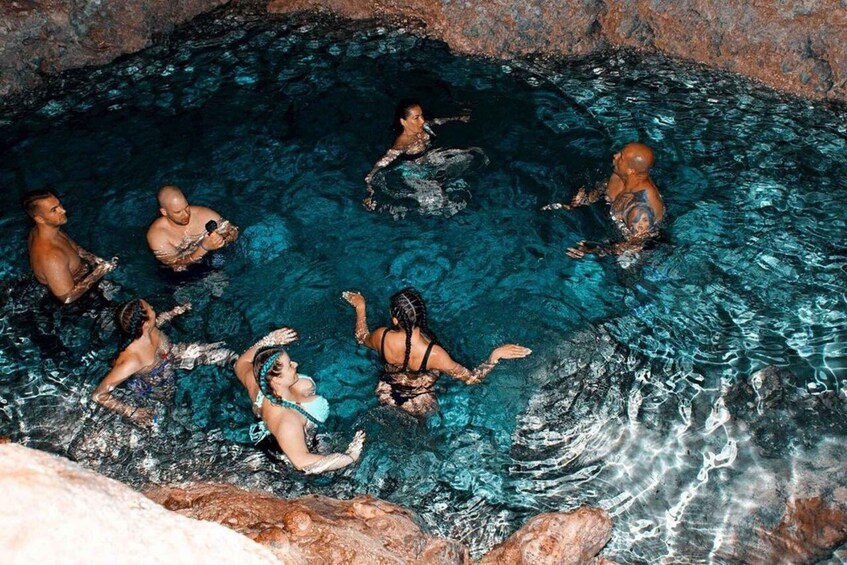 A group of people in a natural pool surrounded by rocky terrain. 2