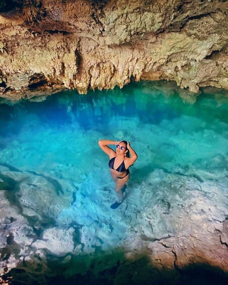 A person in a swimsuit standing in a clear blue pool with rocky walls. 3