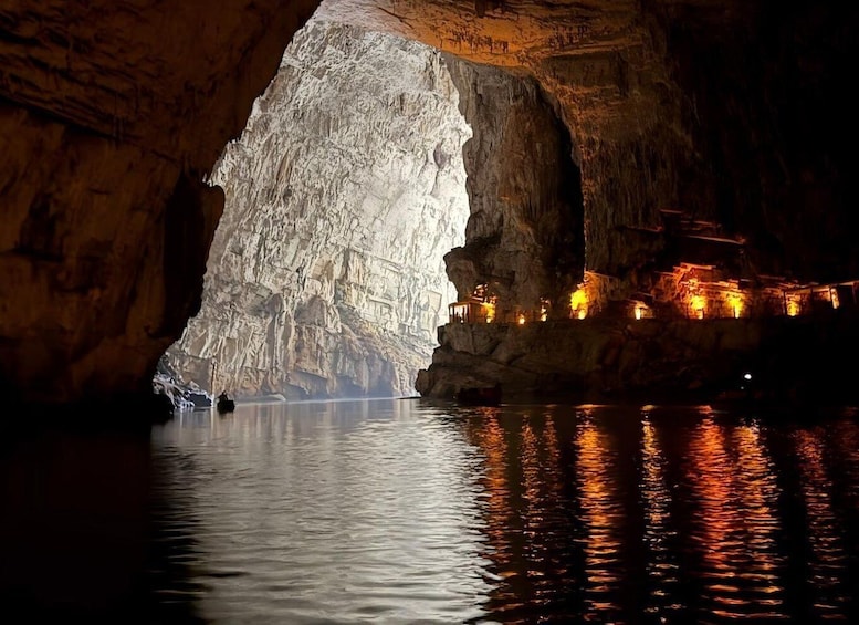 A cave with a large opening, water reflecting lights, and structures built into the cave walls. 1