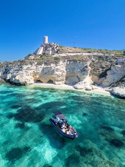 A boat on clear turquoise waters with rocky cliffs and a lighthouse in the background. 5