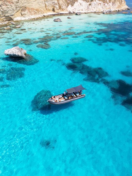 A boat with passengers on a clear turquoise sea with rocky cliffs in the background. 4