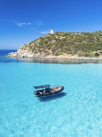 A boat on clear turquoise water with a rocky coastline and a hill with a tower in the background. 3